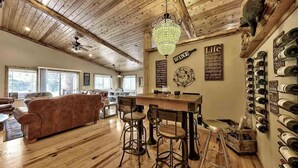 A rustic interior with a wooden ceiling, a chandelier, a bar area with stools, a wine rack, and a sofa. - Cabin retreat with Hot Tub (Truckee)