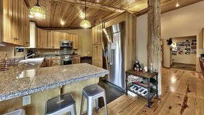 A kitchen with wooden cabinets, granite countertops, stainless steel appliances, and a bar area with stools. - Cabin retreat with Hot Tub (Truckee)