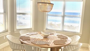 Un coin repas avec une table ronde en bois, des chaises blanches et un luminaire suspendu en fibres tressées.