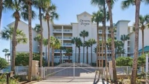 Un hôtel doté d’une entrée sécurisée par un portail, de palmiers et d’une enseigne indiquant « Crystal Dunes ».
