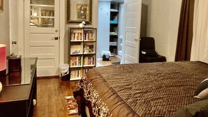 Een slaapkamer met een groot bed, een boekenkast, een deur naar een badkamer en een stoel.