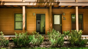 Een houten huis met twee verdiepingen, een veranda, een voordeur en een kleine tuin.