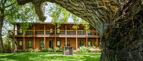 A two-story wooden building with balconies, surrounded by a well-maintained lawn and large trees.