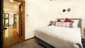 Een slaapkamer met een bed, een plafondventilator, een deur naar een andere kamer en een aan de muur hangend schilderij.