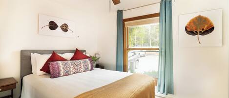 A neatly made bed with a patterned pillow, a ceiling fan, and two framed leaf artworks on the walls.
