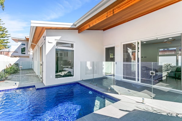 A modern house with a swimming pool, large glass doors, and a wooden ceiling.
