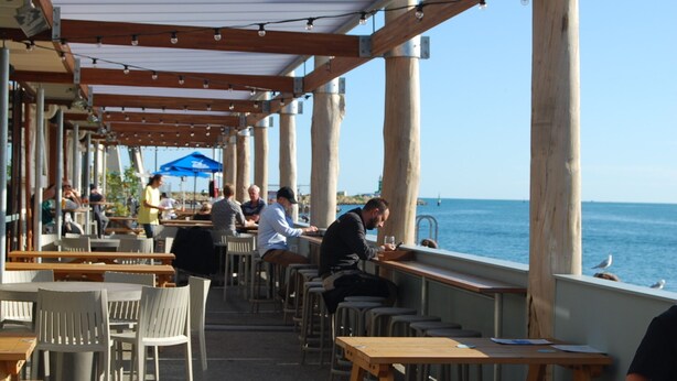 An outdoor café with wooden tables and chairs, overlooking the sea.