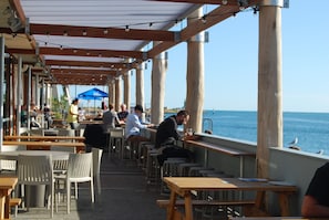 An outdoor café with wooden tables and chairs, overlooking the sea.