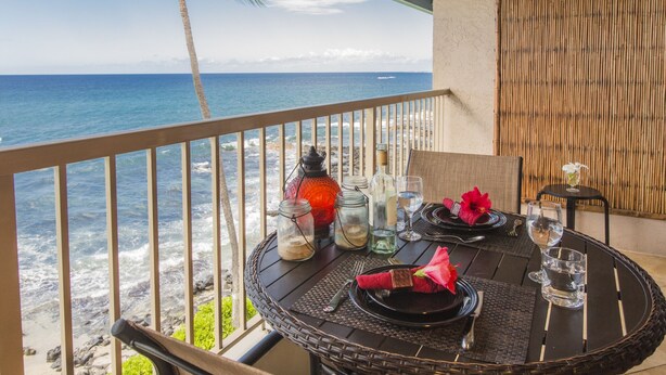 A dining table set on a balcony with a view of the ocean and beach.