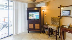 A room with a television, a standing lamp, a wicker chair, a small table, and a ceiling fan.