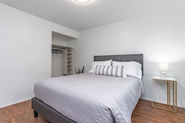 Ein modernes Schlafzimmer mit einem großen Bett, einem Nachttisch mit Lampe und einem Einbauschrank mit Regalen.
