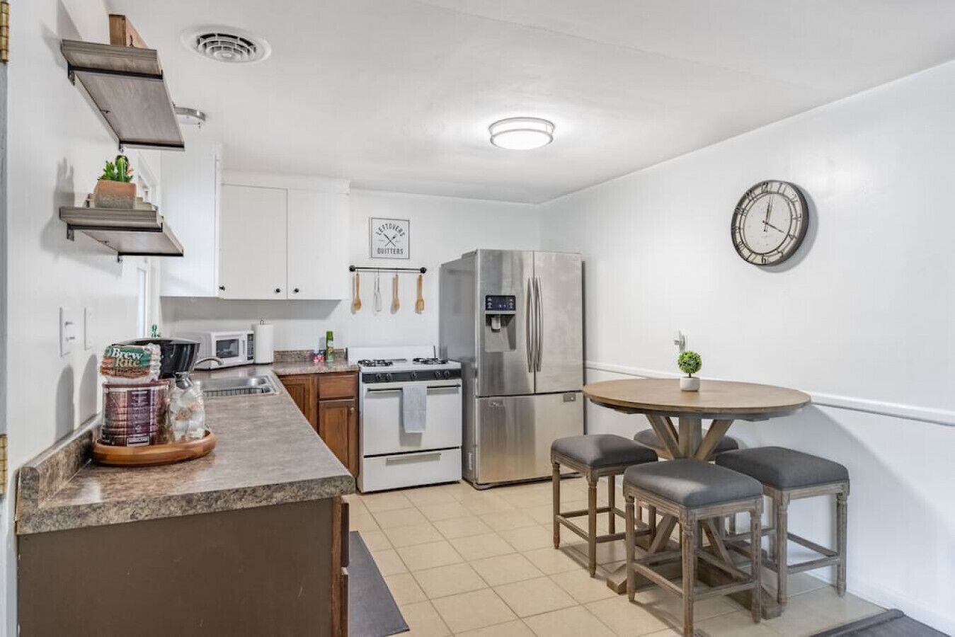 A compact kitchen with a central island, a refrigerator, a stove, and a microwave. There is a small dining area with a table and two chairs.