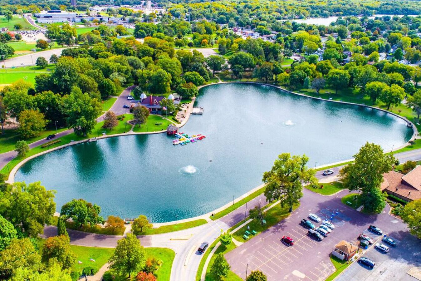 Vue aérienne d’un parc avec un lac, une aire de jeux et un parking.