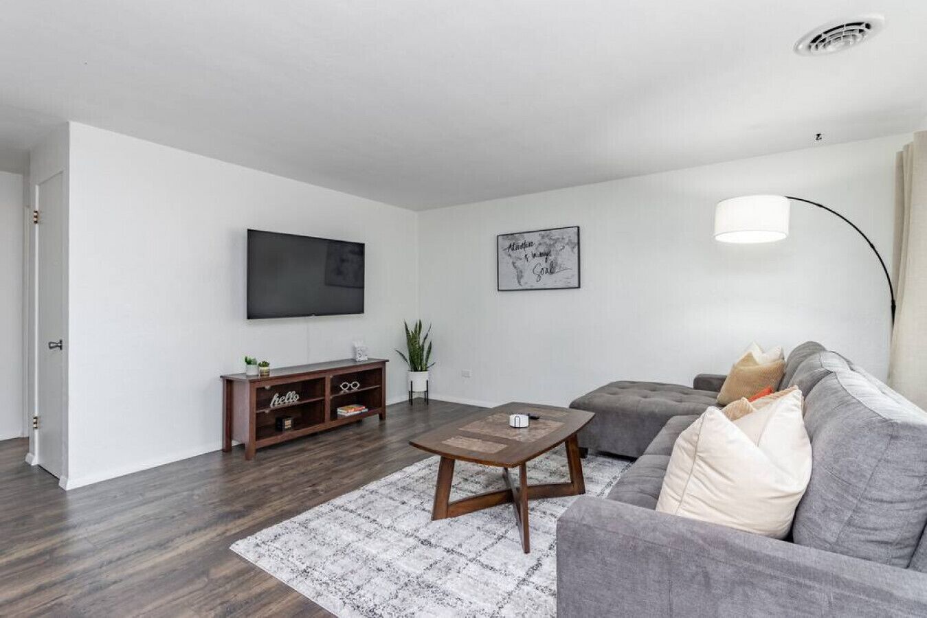 A modern living room with a grey sofa, a wooden coffee table, and a flat-screen TV mounted on the wall.