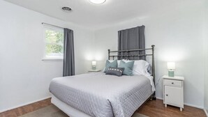 Un dormitorio ordenado con cama, dos mesitas de noche, una ventana con cortinas e iluminación en el techo.