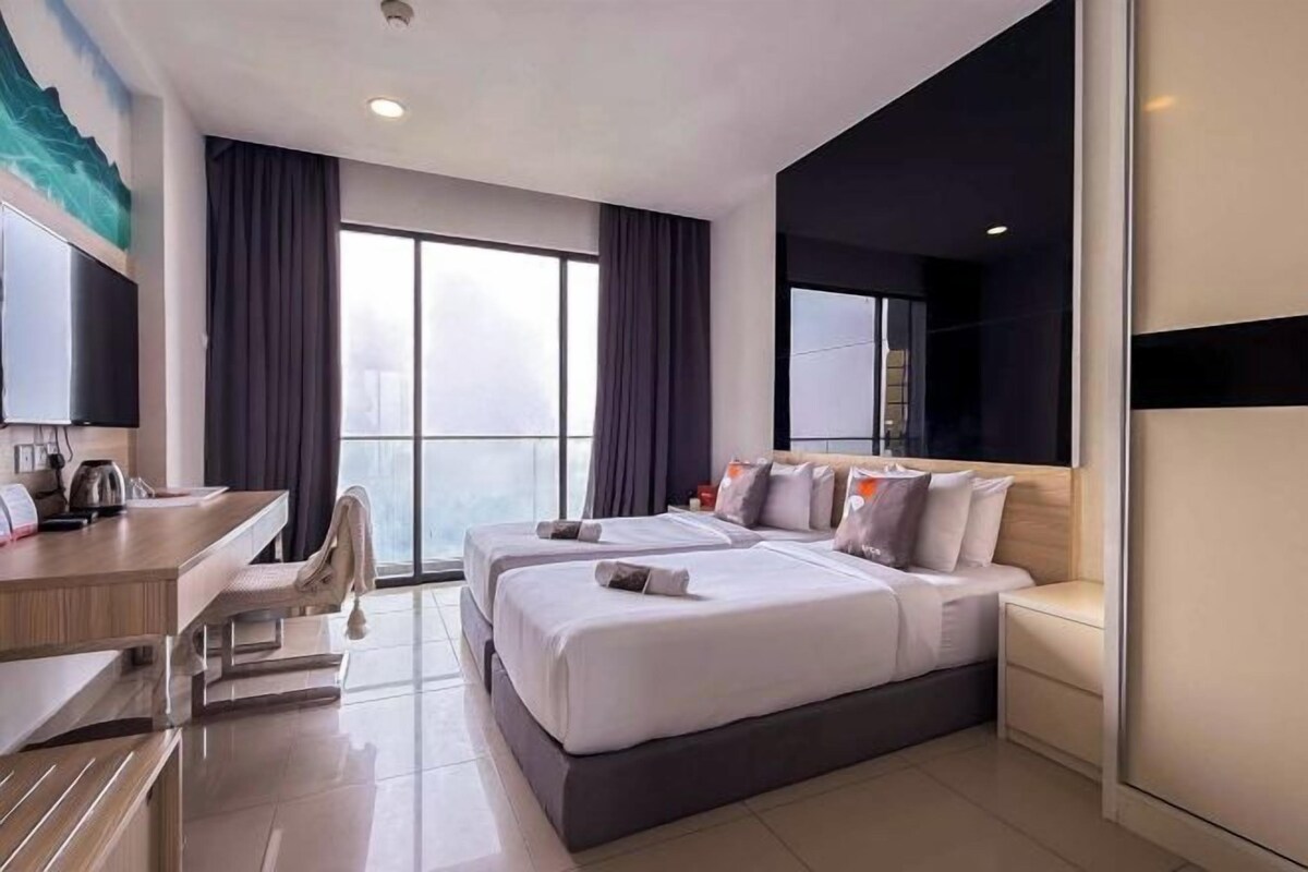 A hotel room with two beds, a desk, a chair, and a large window.