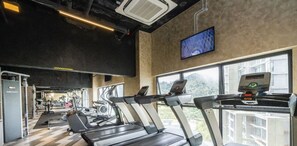Een fitnessruimte met loopbanden, krachttoestellen en een groot raam met uitzicht op groen.