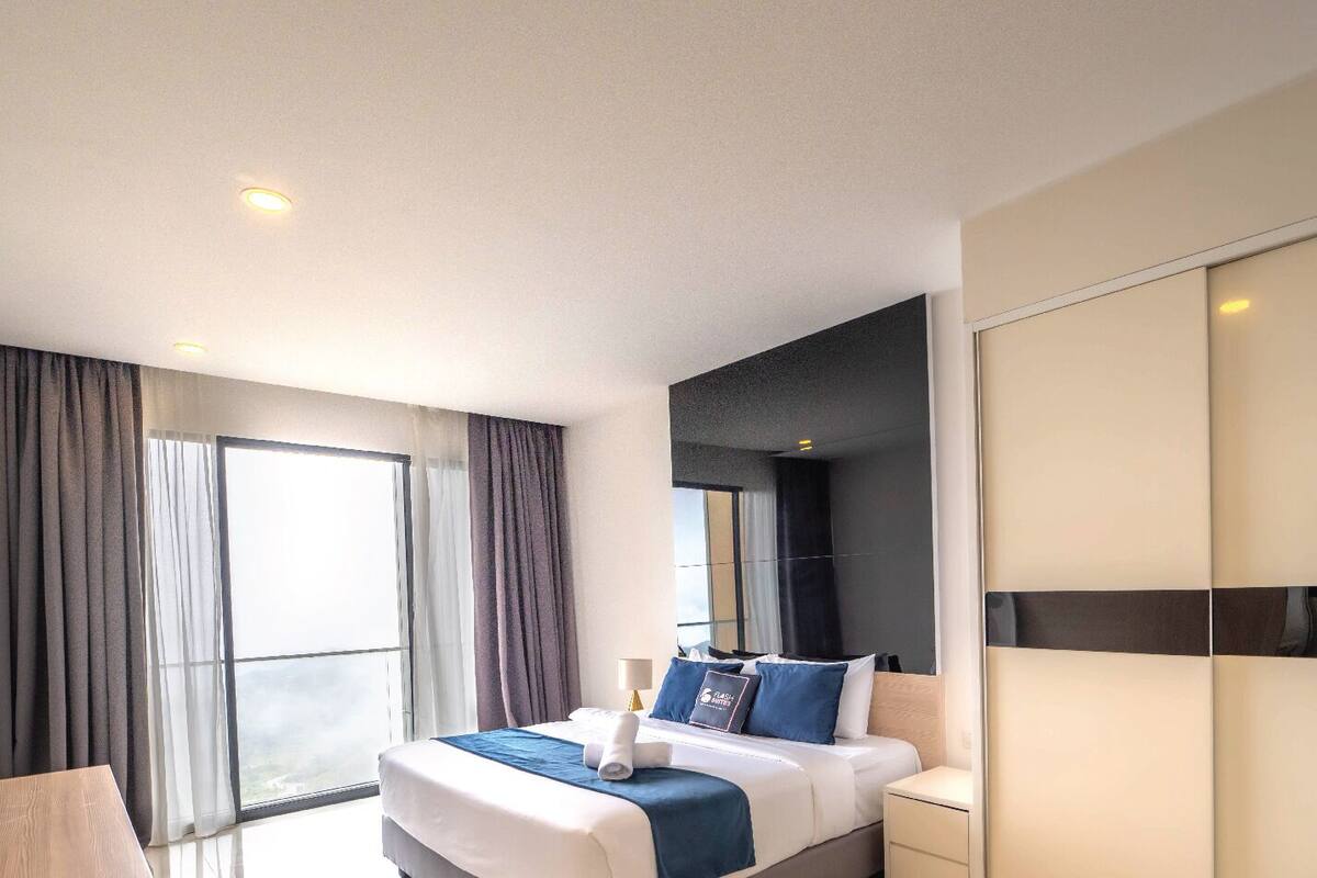 A modern hotel room with a large bed, a wardrobe, and a window with curtains.