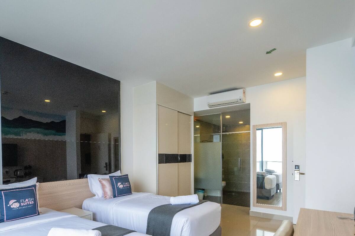 A hotel room with two beds, a shower area, and a desk with a kettle.
