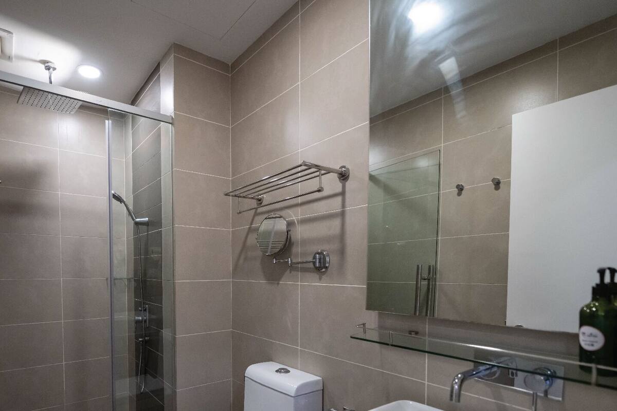A modern bathroom with a glass-enclosed shower, a toilet, a sink with a mirror, and a towel rack.