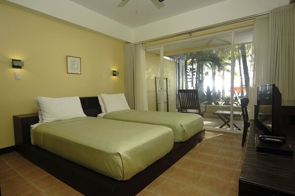 Habitación de hotel con dos camas, televisión y balcón con vistas a palmeras.