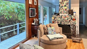 Una sala de estar acogedora con techo de madera, un sofá redondo, chimenea y ventanas grandes con vistas a un jardín.