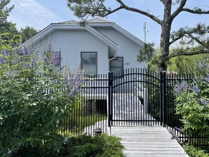 Une maison blanche avec un portail noir et un chemin en bois menant à l’entrée.
