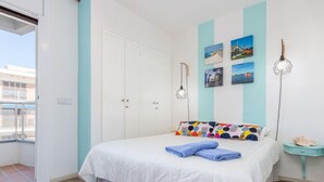 Ein Schlafzimmer mit Bett, Kleiderschrank, Nachttisch und Fenster mit Blick auf Gebäude.