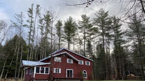 Ein zweistöckiges rotes Haus mit Veranda, umgeben von einem Wald.
