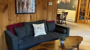 Ein Zimmer mit einem dunkelgrauen Sofa, einem Holztisch und einem gerahmten Bild an der Wand.