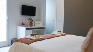 Une chambre moderne avec un grand lit, un téléviseur à écran plat fixé au mur, un bureau avec une chaise et une porte-fenêtre coulissante donnant sur un balcon.