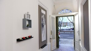 Un pasillo con una puerta blanca, una obra de arte enmarcada y una estantería con adornos.
