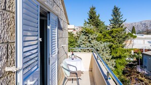 A balcony with a table and chair, a bottle of wine, and a view of trees and buildings. - Cozy Duplex Apartment A2, in a Stone Built House, Sunset Beach Near Dubrovnik (Dubrovnik)