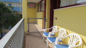 A balcony with a metal gate, two white plastic chairs with blue cushions, and a yellow wall. - Colorful Studio by the Beach-beahost (San Michele al Tagliamento)