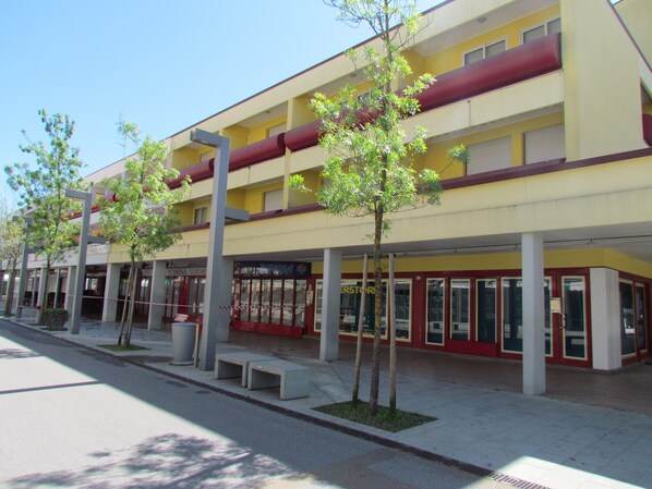 A multi-story building with a yellow facade, large windows, and a red awning. - Colorful Studio by the Beach-beahost (San Michele al Tagliamento)