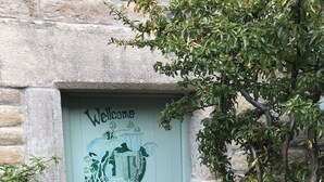 A light green door with a 'Welcome' sign and a coat of arms design, flanked by potted plants.