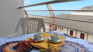 Een balkon met een tafel gedekt voor twee personen, twee kopjes, een zeester en een tafelkleed met een patroon.