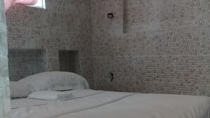 A bedroom with a brick-patterned wall, a bed with white bedding, and a window with a pink curtain. - Villa Julirous Rd, spa and Aparthotel Camp for Vacationers (Boca Chica)