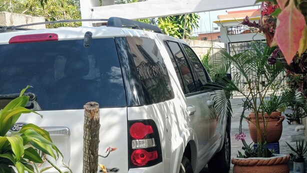 A white SUV parked in a driveway with potted plants and a small table with a cup. - Villa Julirous Rd, spa and Aparthotel Camp for Vacationers (Boca Chica)
