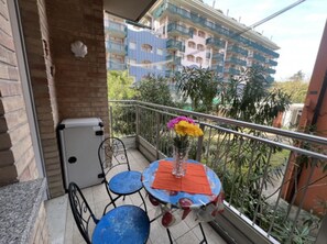 A balcony with a table and chairs, a potted plant, and a view of a multi-story building. - Feel at Home in our Flat - Beahost (San Michele al Tagliamento)