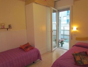 A bedroom with two beds, a wardrobe, and a sliding glass door leading to a balcony.