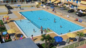A large swimming pool surrounded by sun loungers and umbrellas, with a view of residential buildings in the background. - Poolside Getaway-beahost (Rosolina)