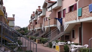 A residential building with multiple balconies, a central staircase, and outdoor seating areas. - Poolside Getaway-beahost (Rosolina)