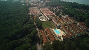 An aerial view of a coastal residential area with a large swimming pool, dense greenery, and a mix of residential buildings. - Poolside Getaway-beahost (Rosolina)