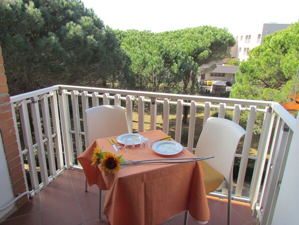 A balcony with a table set for two, chairs, and a view of trees and buildings.
