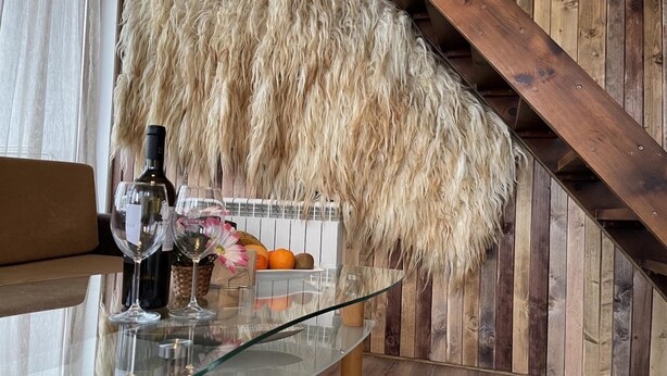 Un comedor con una mesa de vidrio, copas de vino y una cesta de frutas.