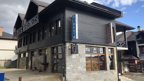 Un edificio con un cartel de alquiler de esquíes, una fachada comercial con varios rótulos y una apariencia de piedra.
