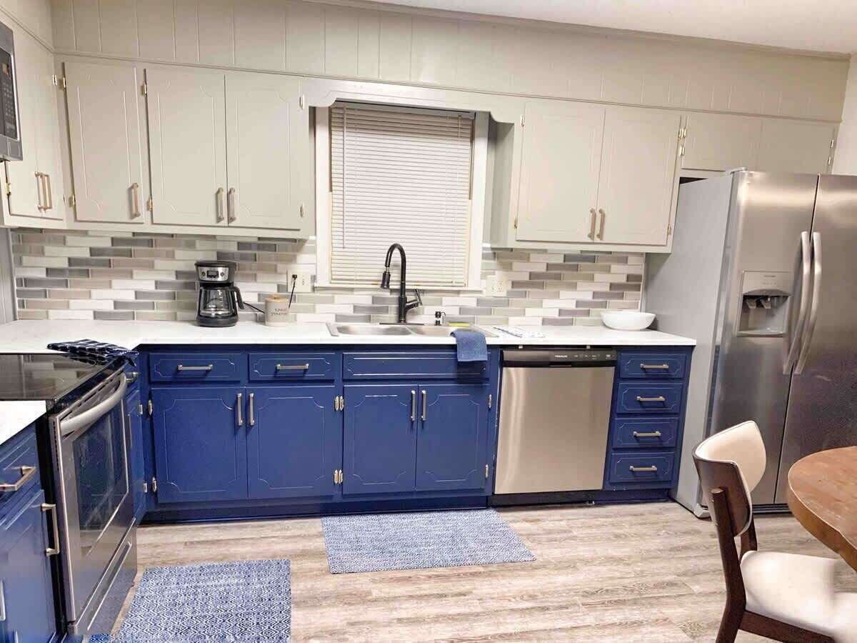 Een keuken met blauwe kastjes, een roestvrijstalen koelkast, een vaatwasser en een koffiezetapparaat.