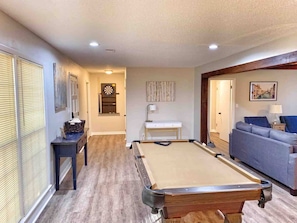 A room with a pool table, a sofa, and a desk with a lamp.