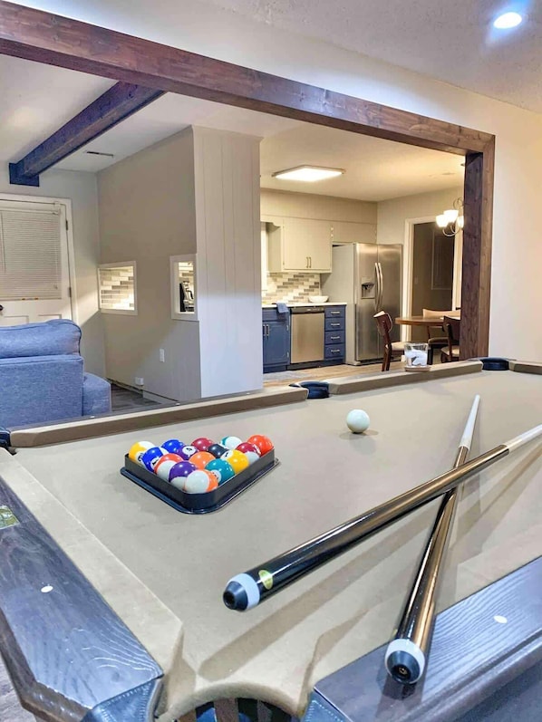 A pool table with balls, a sofa, and a kitchen in the background.